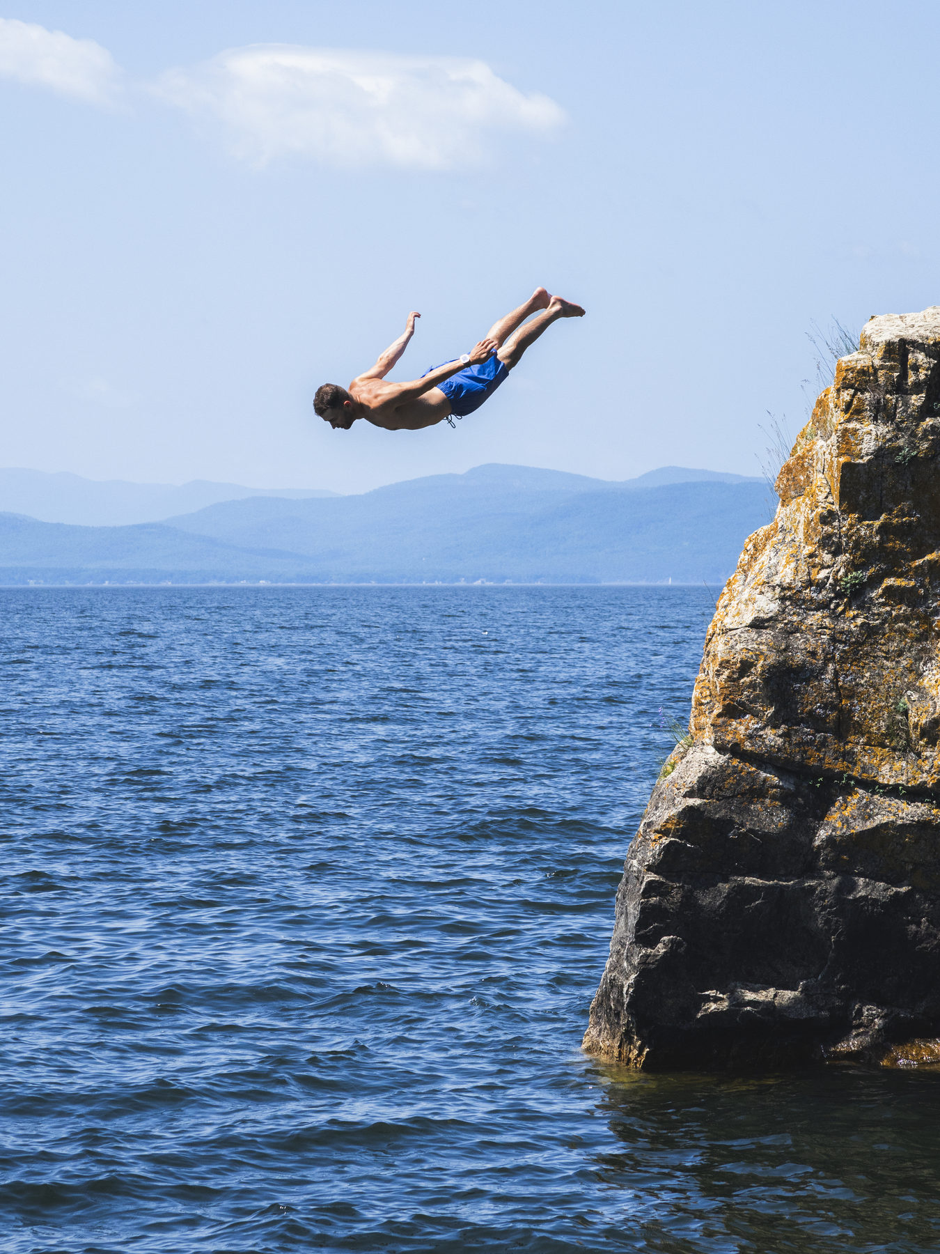 Diving off a cliff into a lake with mountains in the distance